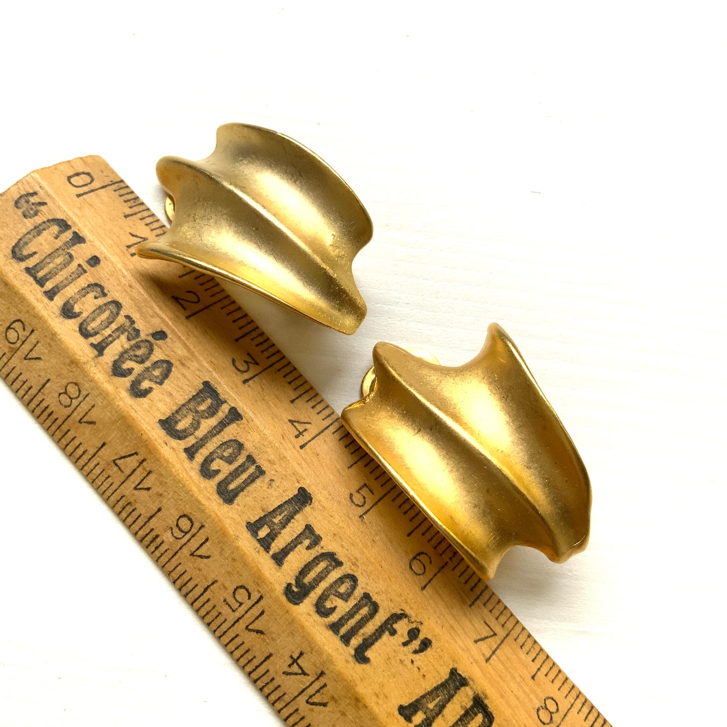 Matte gold-tone clip-on earrings with a simple abstract form. シンプルな抽象的フォルムが印象的な、マットゴールドトーンのクリップイヤリング。