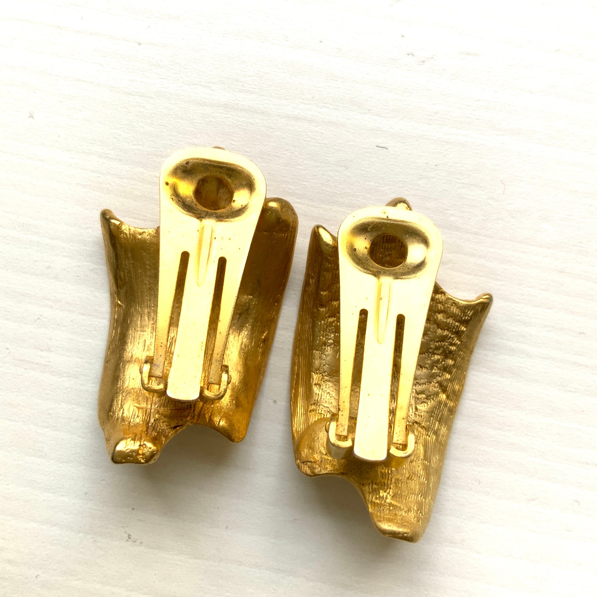 Matte gold-tone clip-on earrings with a simple abstract form. シンプルな抽象的フォルムが印象的な、マットゴールドトーンのクリップイヤリング。