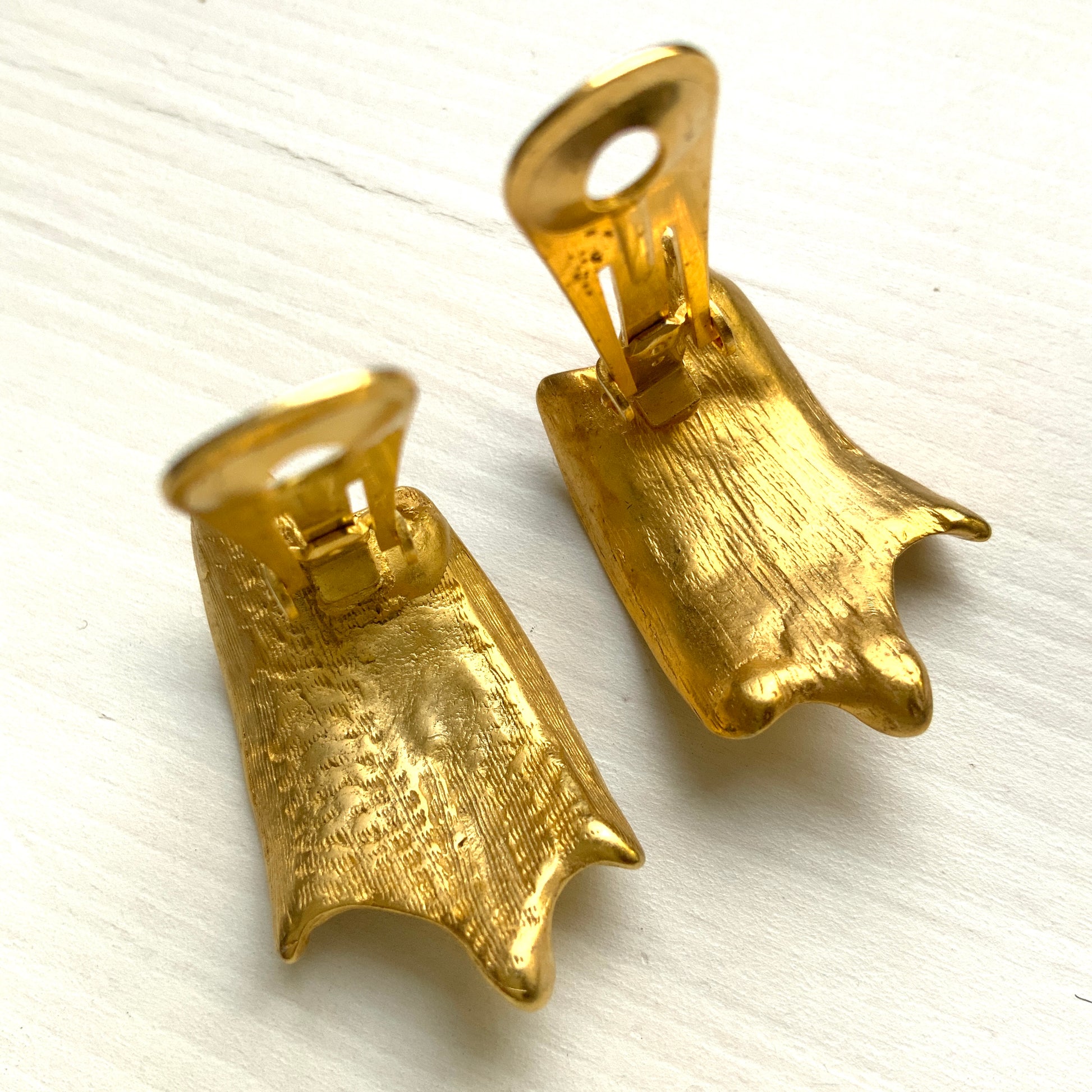 Matte gold-tone clip-on earrings with a simple abstract form. シンプルな抽象的フォルムが印象的な、マットゴールドトーンのクリップイヤリング。