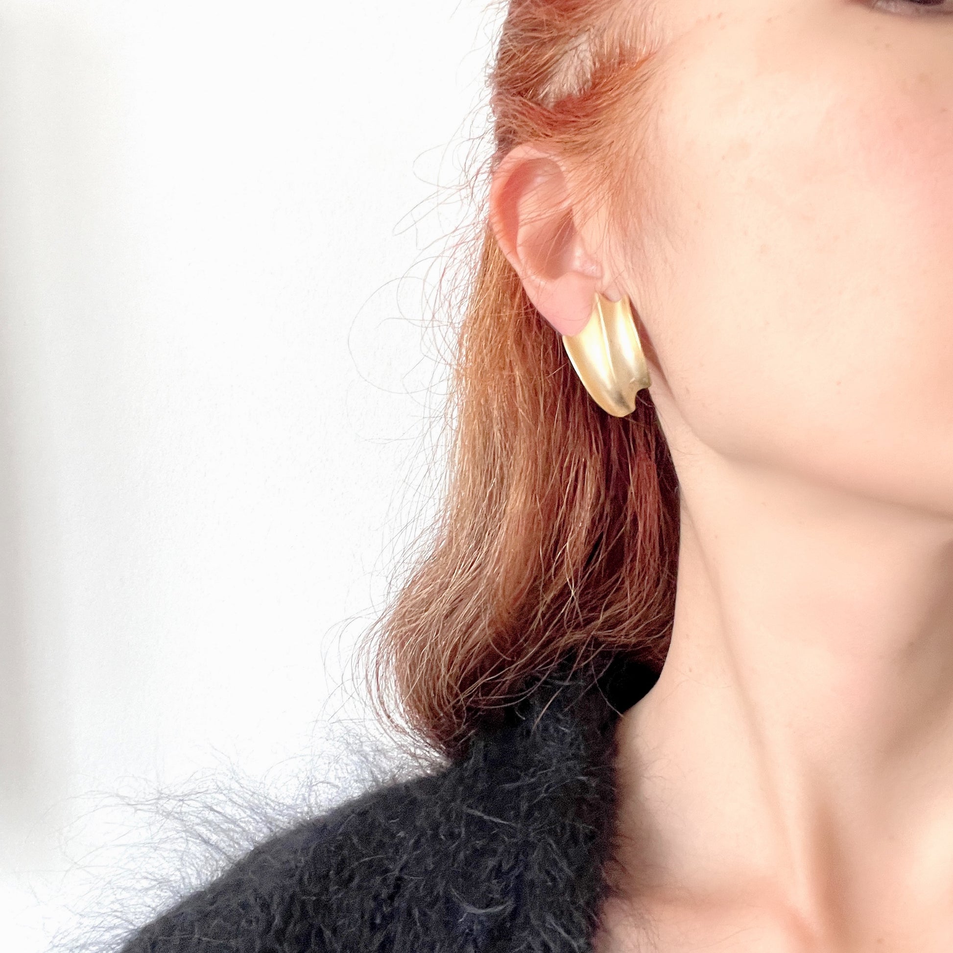 Matte gold-tone clip-on earrings with a simple abstract form. シンプルな抽象的フォルムが印象的な、マットゴールドトーンのクリップイヤリング。