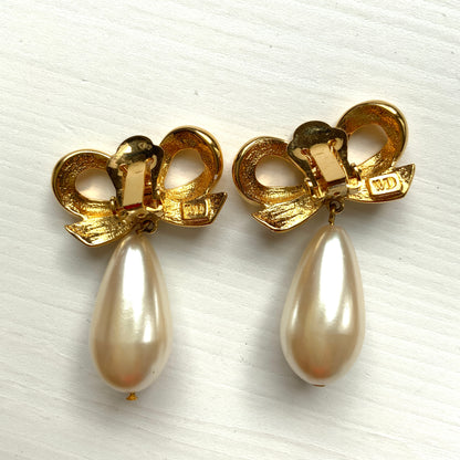 A pair of clip-on earrings featuring a bow motif in gold-tone metal, with large teardrop-shaped faux pearls that sway beautifully as you move. ゴールドトーンメタルのリボンモチーフに、大ぶりのティアドロップ型フォーパールが揺れるクリップイヤリング。 