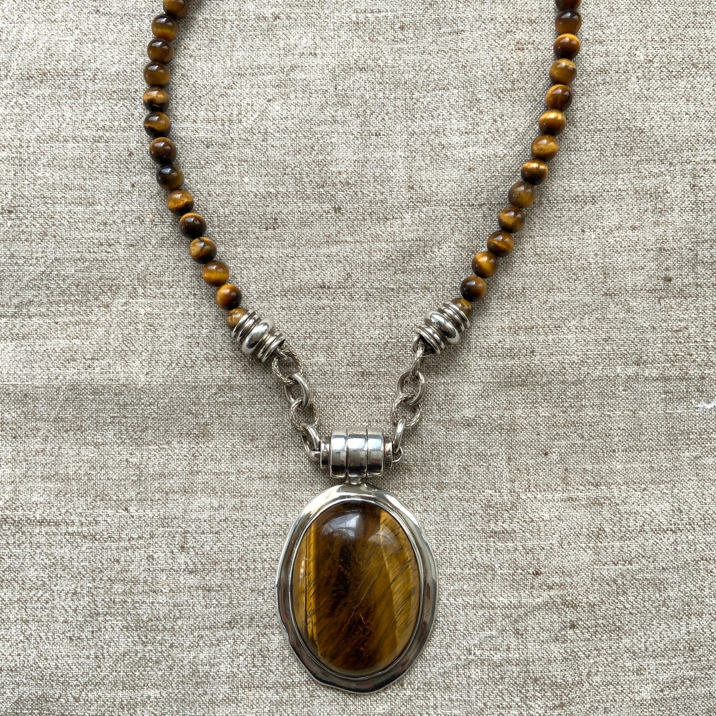 A bold oval-shaped tiger's eye stone takes centre stage in this striking silver necklace by Joseph Esposito. 大ぶりのオーバル型タイガーアイが印象的な、ジョセフ・エスポジートによるシルバーネックレス。