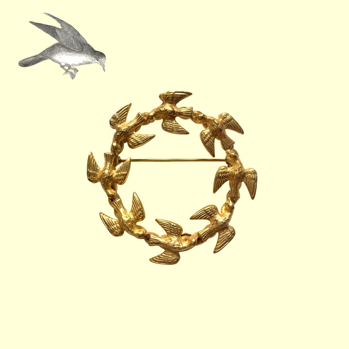 A gold-tone wreath brooch formed by a circle of small birds in flight. ゴールドトーンメタルでつくられた、鳥たちのリースブローチ。 