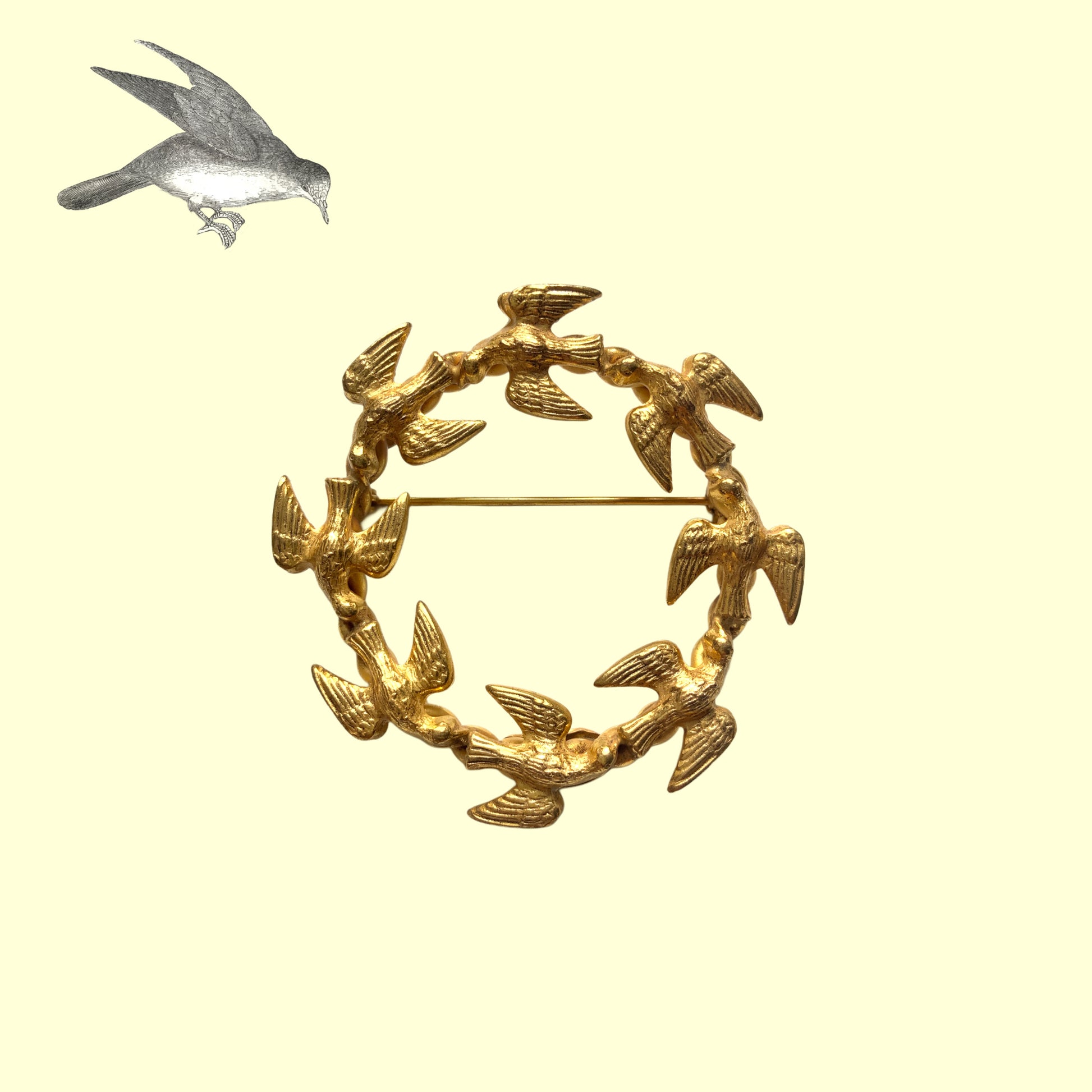 A gold-tone wreath brooch formed by a circle of small birds in flight. ゴールドトーンメタルでつくられた、鳥たちのリースブローチ。 