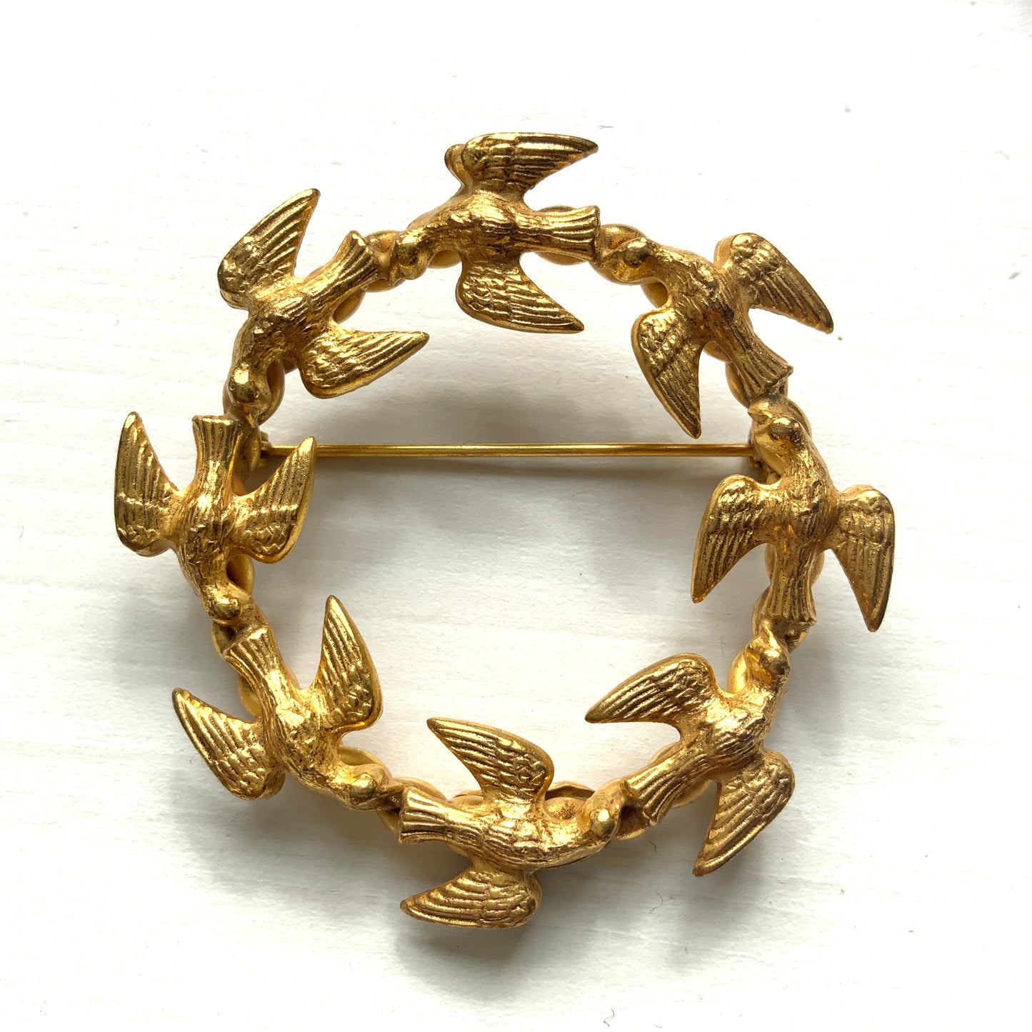 A gold-tone wreath brooch formed by a circle of small birds in flight. ゴールドトーンメタルでつくられた、鳥たちのリースブローチ。 