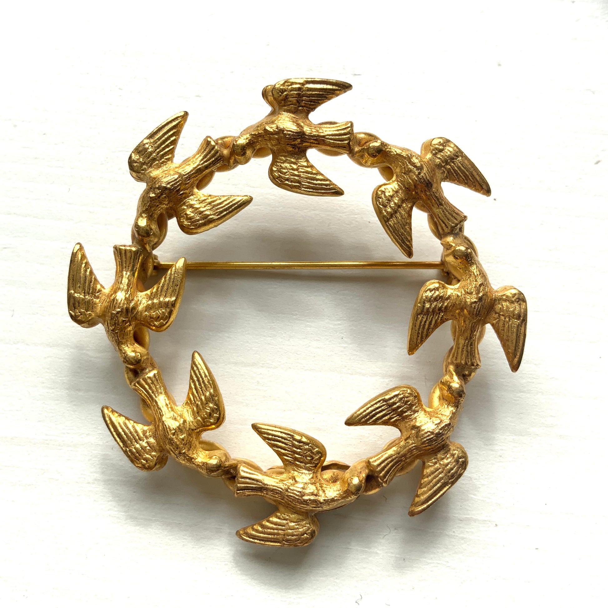A gold-tone wreath brooch formed by a circle of small birds in flight. ゴールドトーンメタルでつくられた、鳥たちのリースブローチ。 