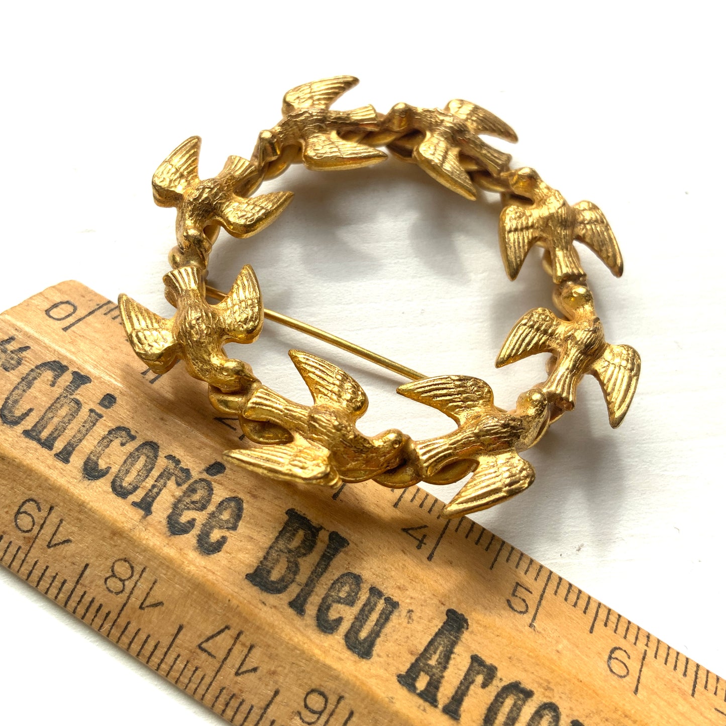 A gold-tone wreath brooch formed by a circle of small birds in flight. ゴールドトーンメタルでつくられた、鳥たちのリースブローチ。 