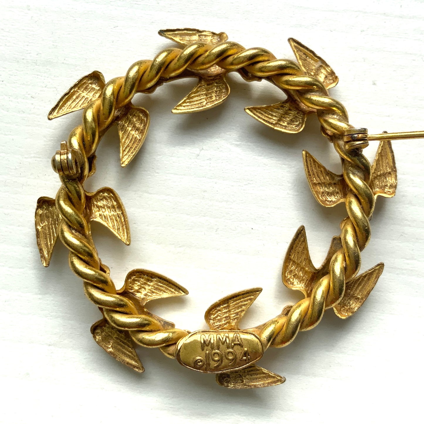 A gold-tone wreath brooch formed by a circle of small birds in flight. ゴールドトーンメタルでつくられた、鳥たちのリースブローチ。 