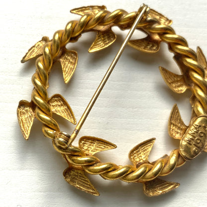 A gold-tone wreath brooch formed by a circle of small birds in flight. ゴールドトーンメタルでつくられた、鳥たちのリースブローチ。 