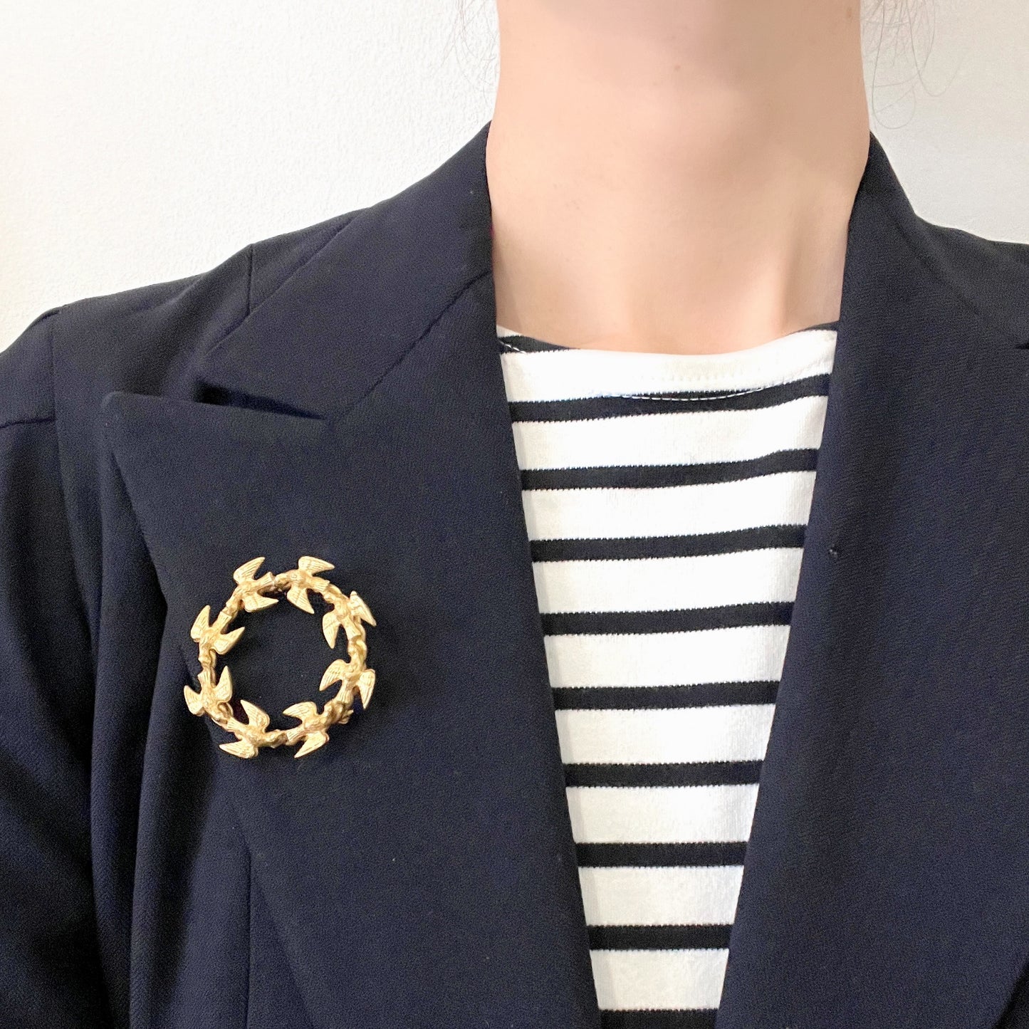 A gold-tone wreath brooch formed by a circle of small birds in flight. ゴールドトーンメタルでつくられた、鳥たちのリースブローチ。 