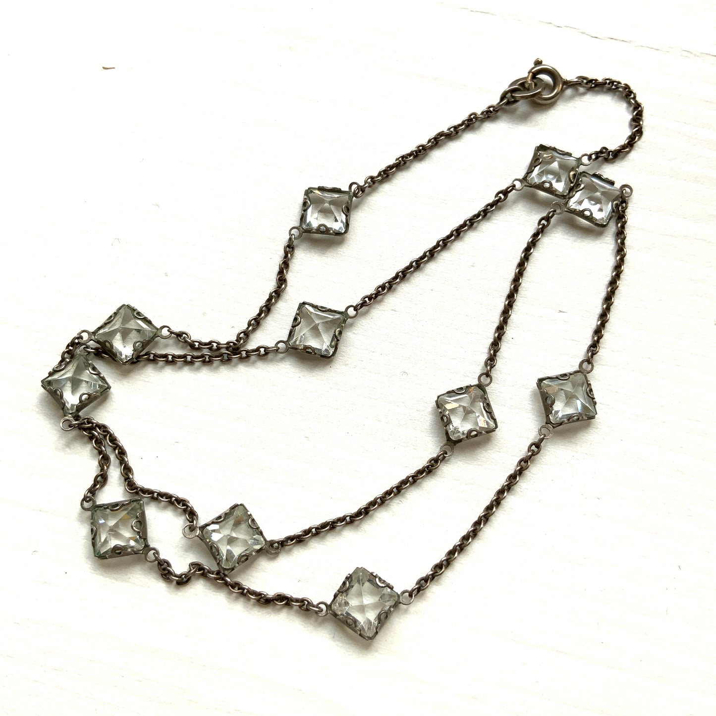 Platinon necklace set with diamond-shaped clear glass stones placed at intervals along the chain. ダイヤ型のクリアグラスがとびとびについたプラチノンのネックレス。