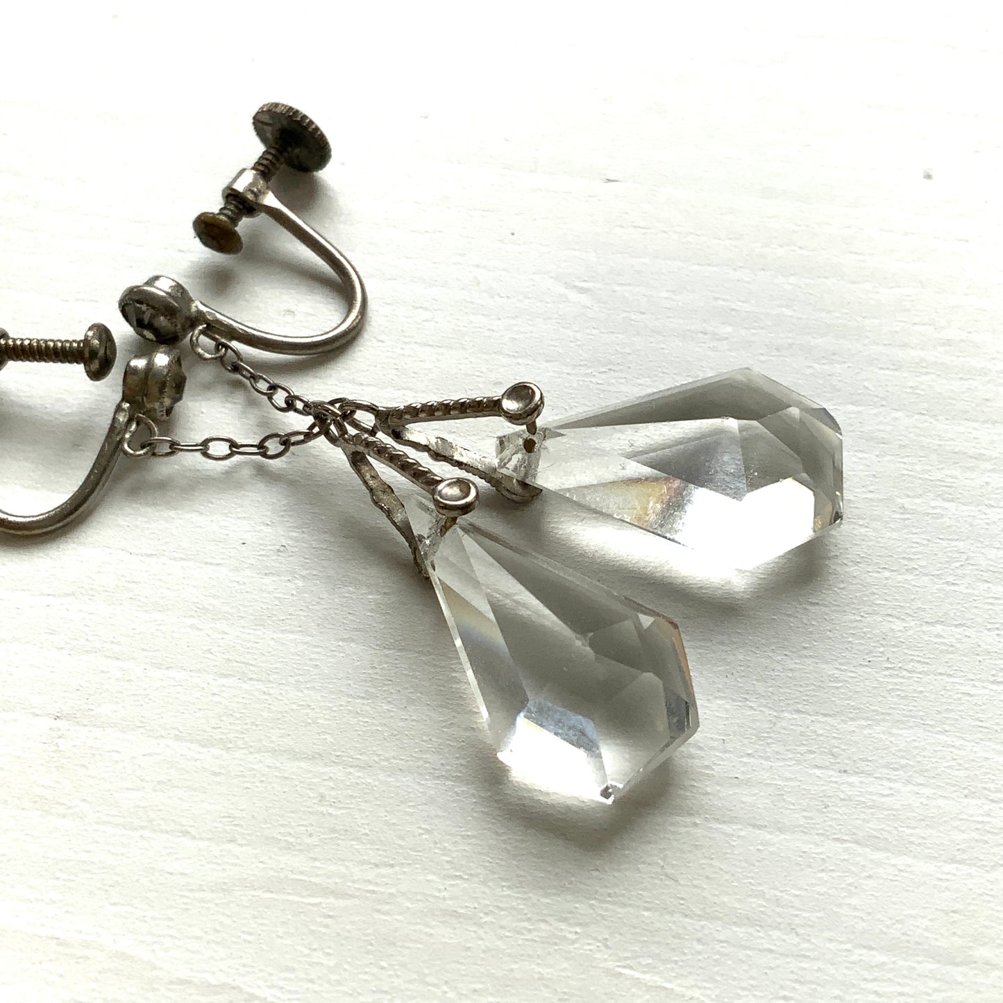 Screw-back earrings featuring clear faceted glass in a unique triangular form. ユニークな三角フォルムのファセットグラスが揺れる、スクリューイヤリング。