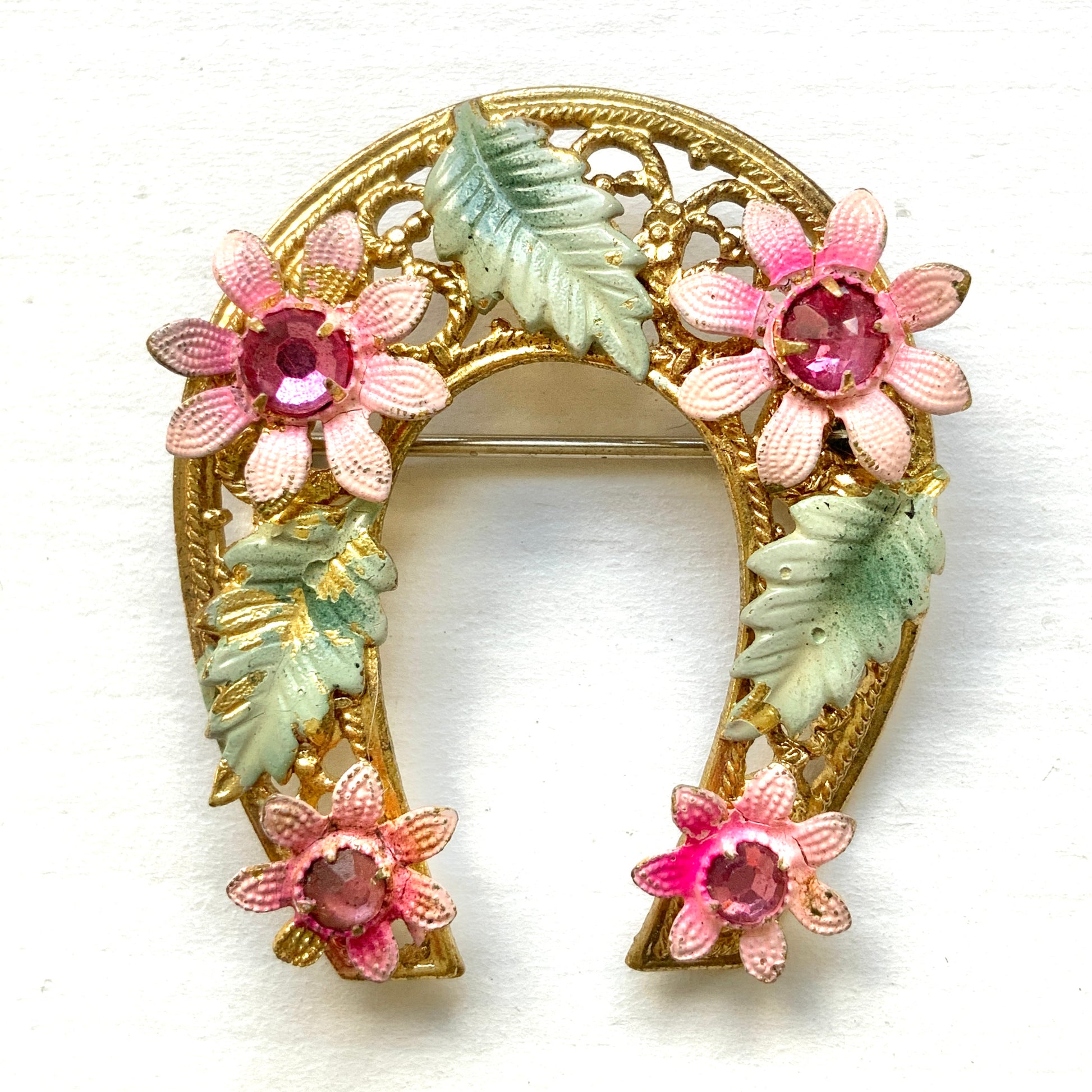 A horseshoe motif brooch adorned with pink enamel flowers. ピンクのエナメルのお花が飾られた、馬蹄モチーフのブローチ。 