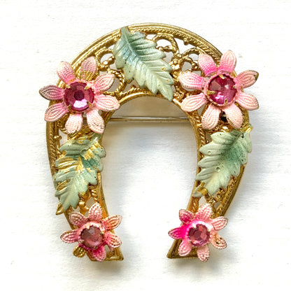 A horseshoe motif brooch adorned with pink enamel flowers. ピンクのエナメルのお花が飾られた、馬蹄モチーフのブローチ。 