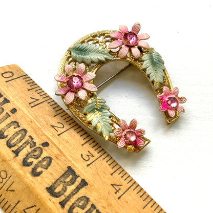 A horseshoe motif brooch adorned with pink enamel flowers. ピンクのエナメルのお花が飾られた、馬蹄モチーフのブローチ。 
