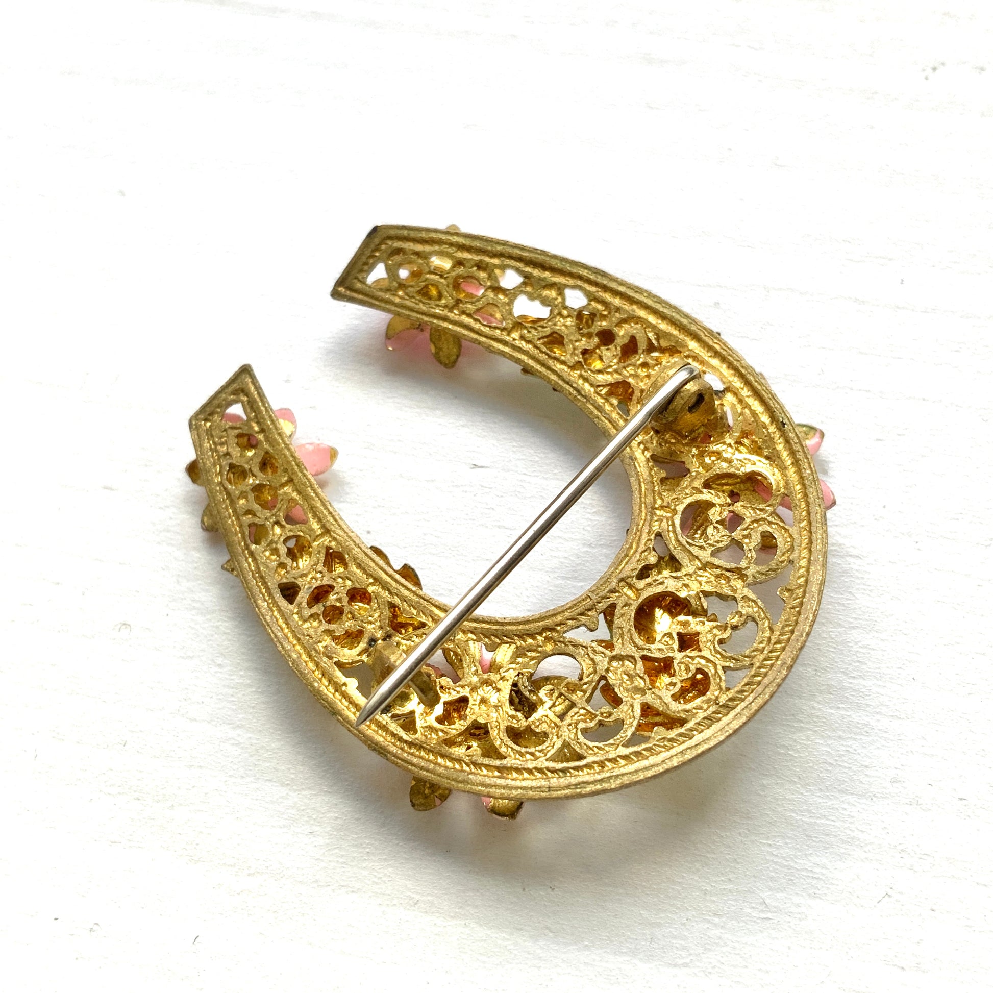 A horseshoe motif brooch adorned with pink enamel flowers. ピンクのエナメルのお花が飾られた、馬蹄モチーフのブローチ。 