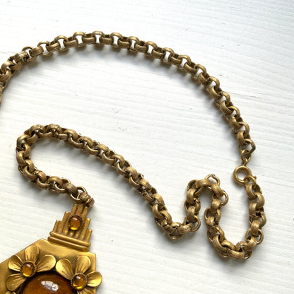 A bright orange cabochon glass, like a little sun, is surrounded by gold-tone metal flowers in this stunning necklace. お日様のように明るいオレンジのカボショングラスを、ゴールドトーンメタルのお花がぐるりと囲んだネックレス。 