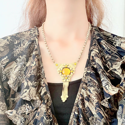 A bright orange cabochon glass, like a little sun, is surrounded by gold-tone metal flowers in this stunning necklace. お日様のように明るいオレンジのカボショングラスを、ゴールドトーンメタルのお花がぐるりと囲んだネックレス。 