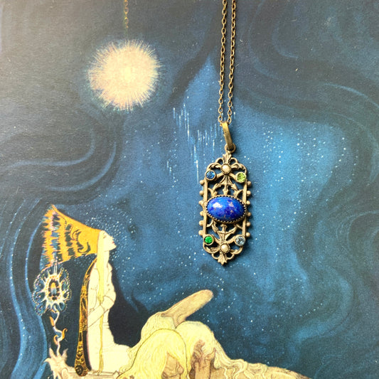 A delicate filigree pendant necklace adorned with a lapis glass cabochon, colourful rhinestones, and seed glass pearls. 繊細なフィリグリーのプレートに、ラピスグラスのカボションとカラフルなラインストーン、シードグラスパールがあしらわれたペンダントネックレス。 