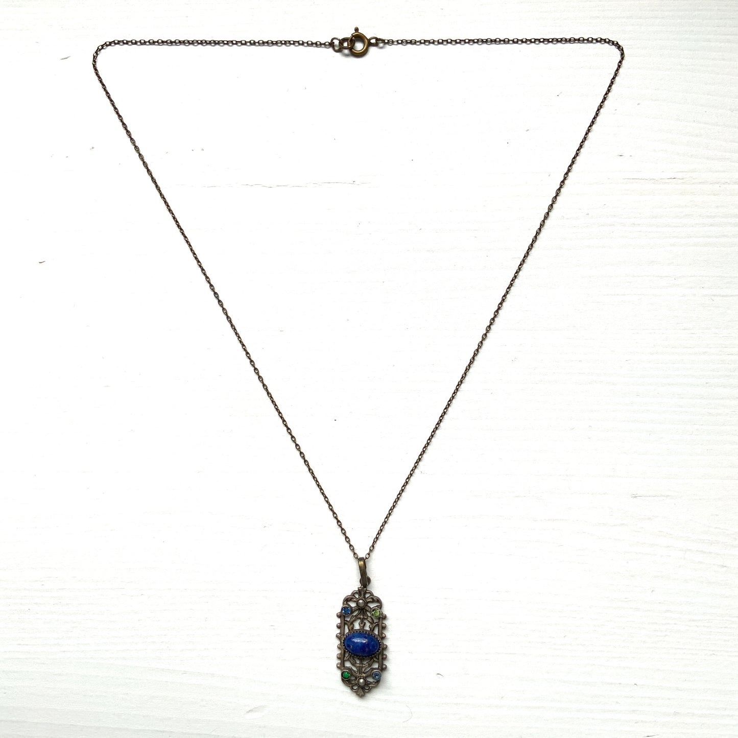 A delicate filigree pendant necklace adorned with a lapis glass cabochon, colourful rhinestones, and seed glass pearls. 繊細なフィリグリーのプレートに、ラピスグラスのカボションとカラフルなラインストーン、シードグラスパールがあしらわれたペンダントネックレス。 