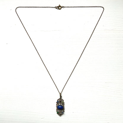 A delicate filigree pendant necklace adorned with a lapis glass cabochon, colourful rhinestones, and seed glass pearls. 繊細なフィリグリーのプレートに、ラピスグラスのカボションとカラフルなラインストーン、シードグラスパールがあしらわれたペンダントネックレス。 