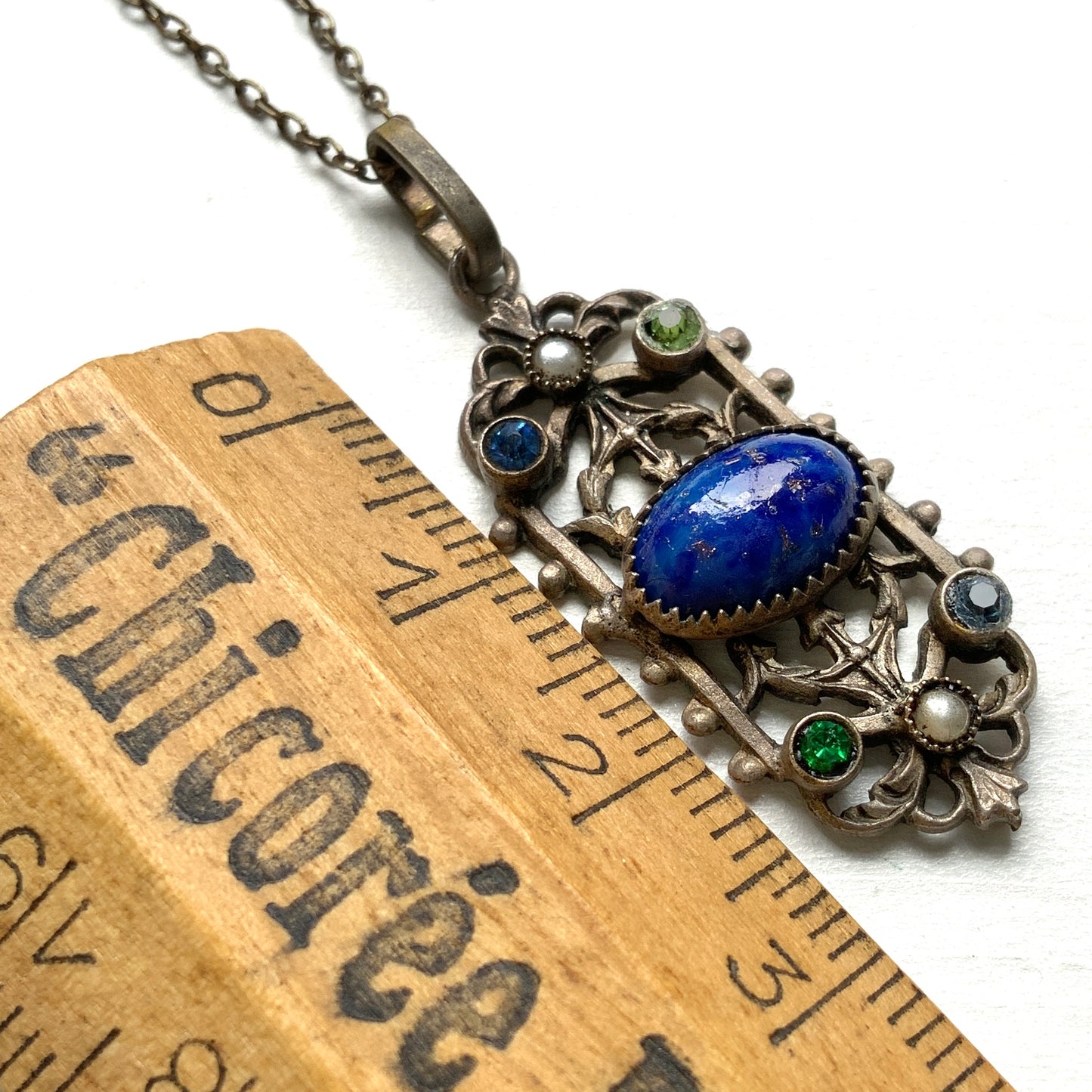 A delicate filigree pendant necklace adorned with a lapis glass cabochon, colourful rhinestones, and seed glass pearls. 繊細なフィリグリーのプレートに、ラピスグラスのカボションとカラフルなラインストーン、シードグラスパールがあしらわれたペンダントネックレス。 