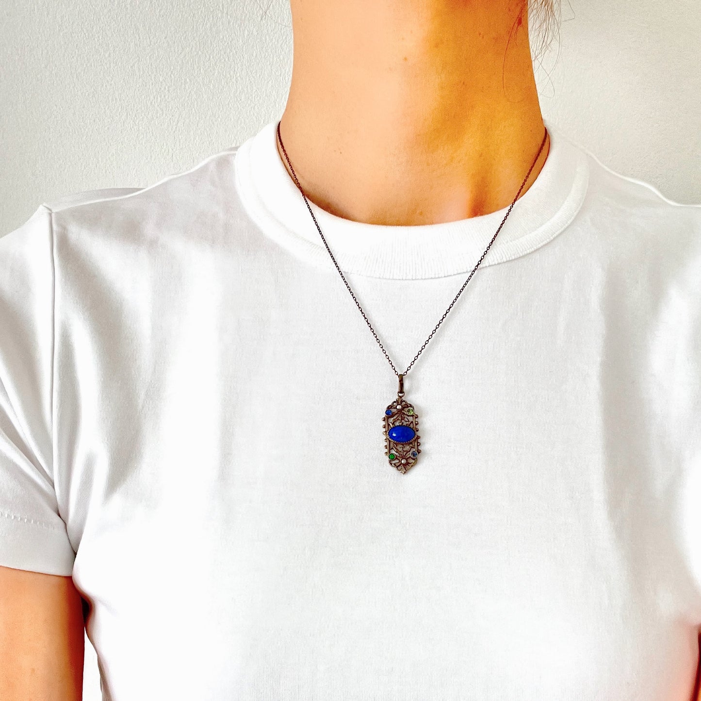 A delicate filigree pendant necklace adorned with a lapis glass cabochon, colourful rhinestones, and seed glass pearls. 繊細なフィリグリーのプレートに、ラピスグラスのカボションとカラフルなラインストーン、シードグラスパールがあしらわれたペンダントネックレス。 