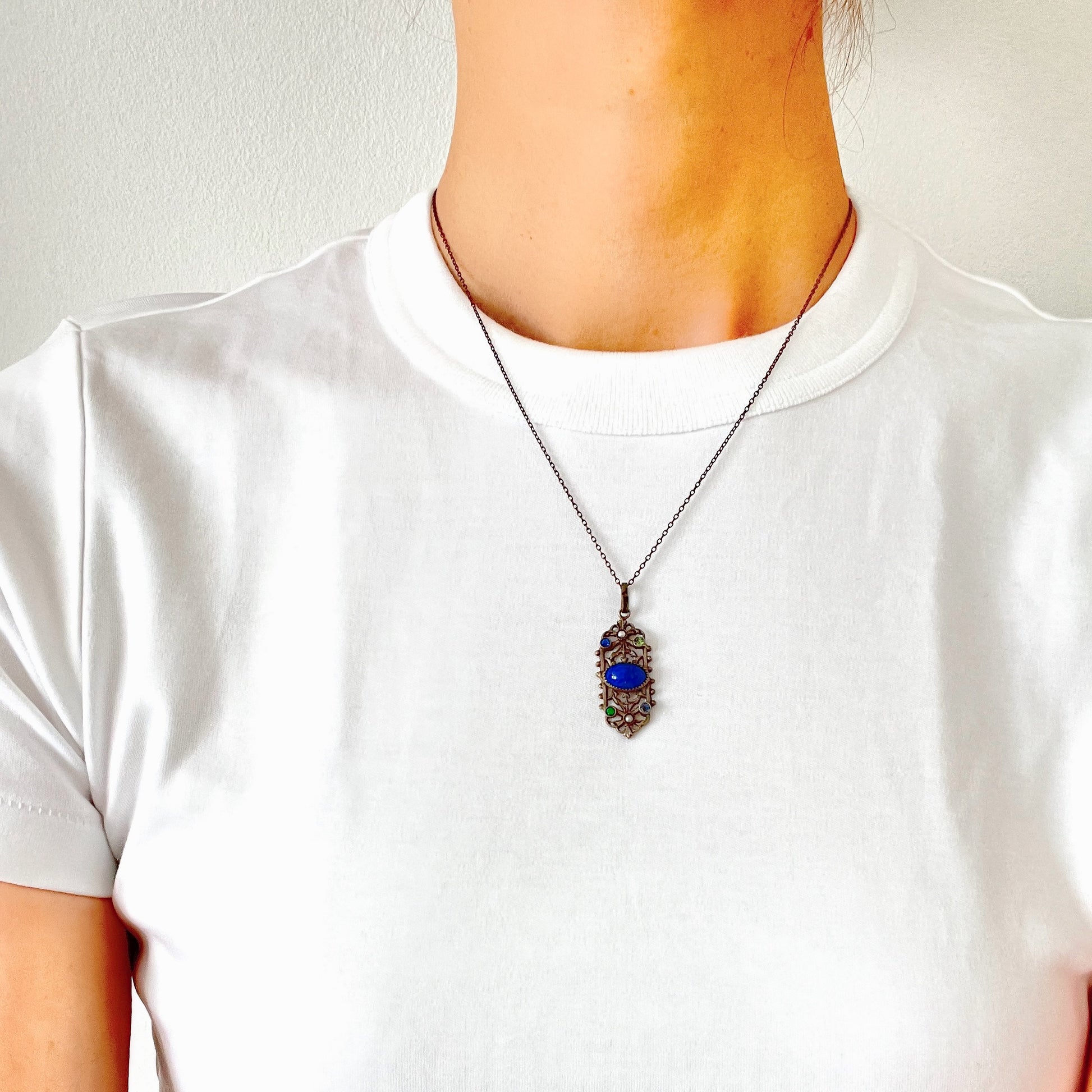 A delicate filigree pendant necklace adorned with a lapis glass cabochon, colourful rhinestones, and seed glass pearls. 繊細なフィリグリーのプレートに、ラピスグラスのカボションとカラフルなラインストーン、シードグラスパールがあしらわれたペンダントネックレス。 