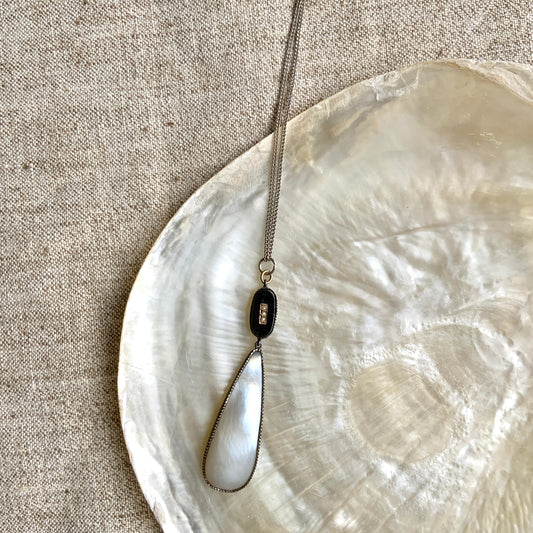 A silver necklace featuring onyx-like black glass paired with a teardrop of smooth, lustrous mother of pearl. オニキスのような艶をもつブラックグラスと、滑らかな光沢が美しいマザーオブパールのティアドロップを組み合わせた、シルバーネックレス。 