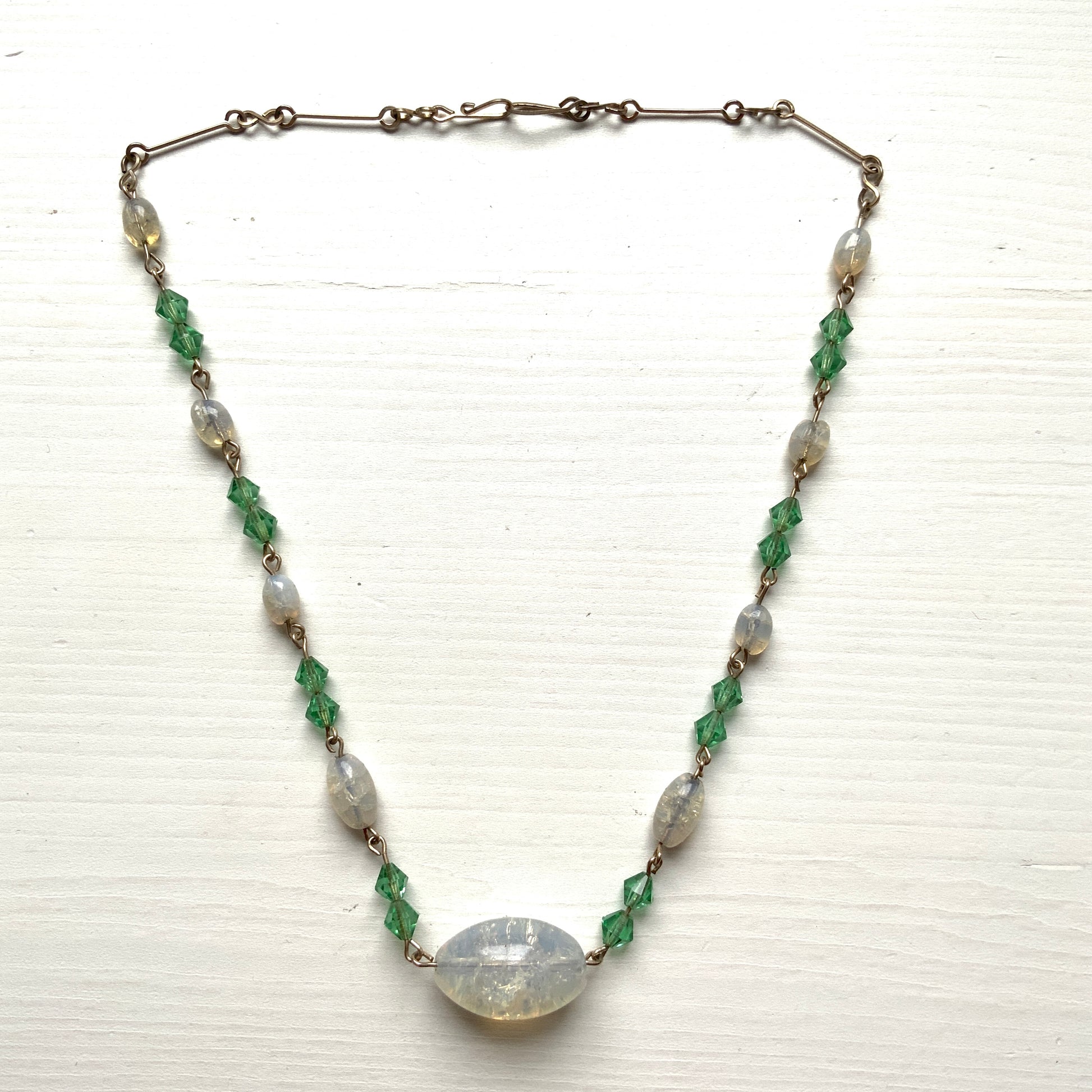 An opalescent crackle glass necklace accented with small green glass beads. オパルセントクラックルグラスに小さなグリーングラスを添えたネックレス。