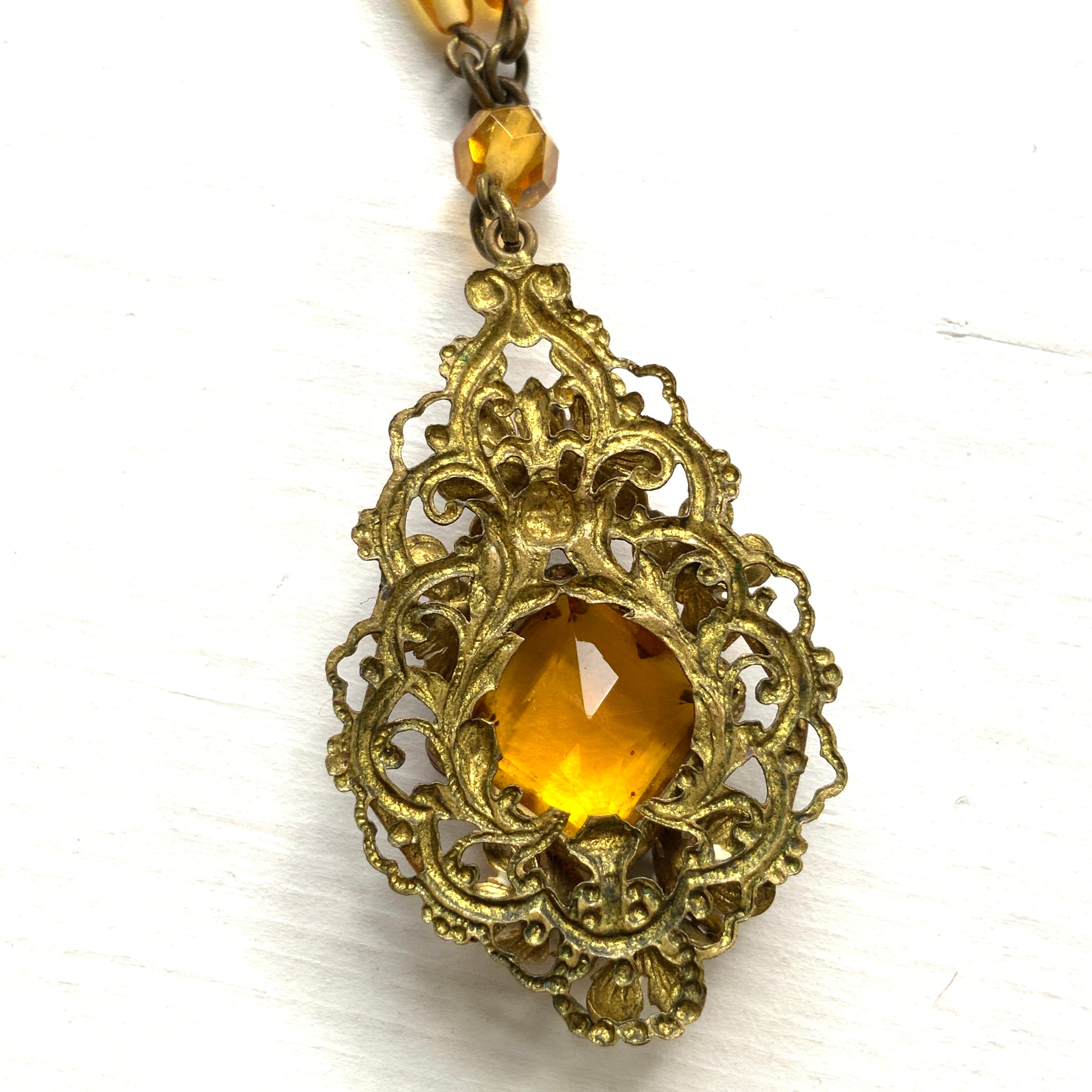 A Czech-made necklace featuring a diamond-shaped amber glass stone encircled by vivid orange enamel flowers. ダイヤ型のアンバーグラスをオレンジ色のエナメルフラワーが取り囲むチェコ製のネックレス。 