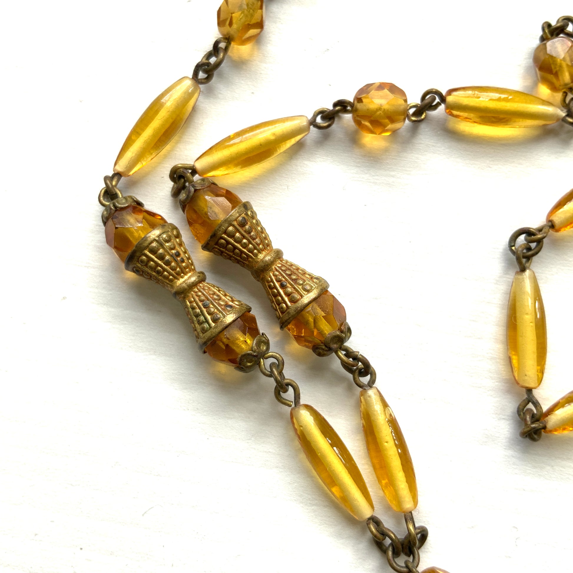 A Czech-made necklace featuring a diamond-shaped amber glass stone encircled by vivid orange enamel flowers. ダイヤ型のアンバーグラスをオレンジ色のエナメルフラワーが取り囲むチェコ製のネックレス。 