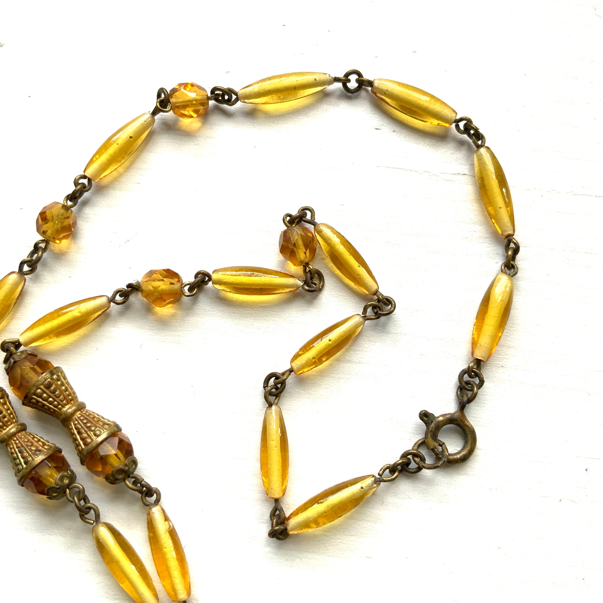 A Czech-made necklace featuring a diamond-shaped amber glass stone encircled by vivid orange enamel flowers. ダイヤ型のアンバーグラスをオレンジ色のエナメルフラワーが取り囲むチェコ製のネックレス。 