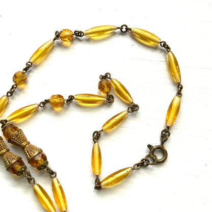 A Czech-made necklace featuring a diamond-shaped amber glass stone encircled by vivid orange enamel flowers. ダイヤ型のアンバーグラスをオレンジ色のエナメルフラワーが取り囲むチェコ製のネックレス。 