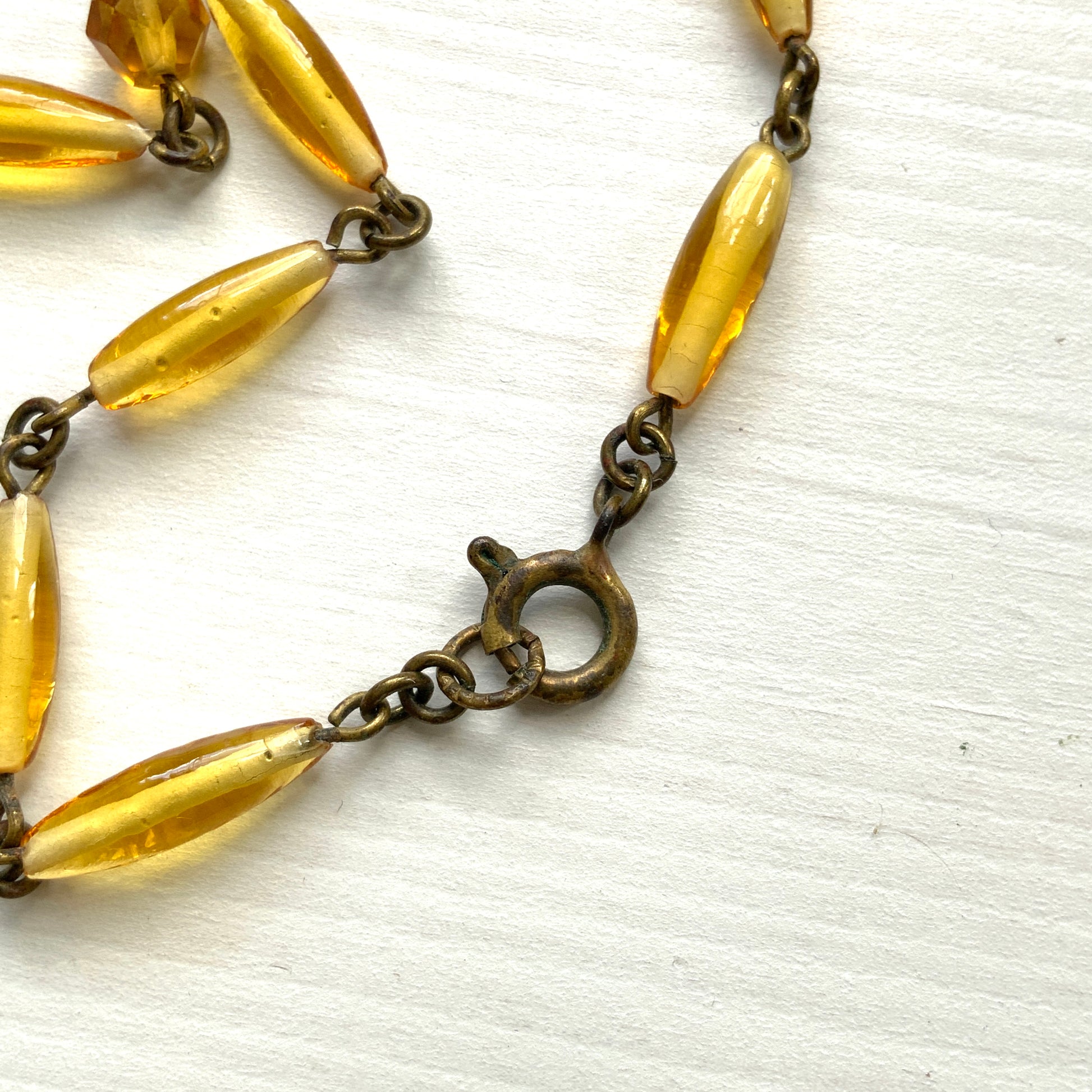 A Czech-made necklace featuring a diamond-shaped amber glass stone encircled by vivid orange enamel flowers. ダイヤ型のアンバーグラスをオレンジ色のエナメルフラワーが取り囲むチェコ製のネックレス。 
