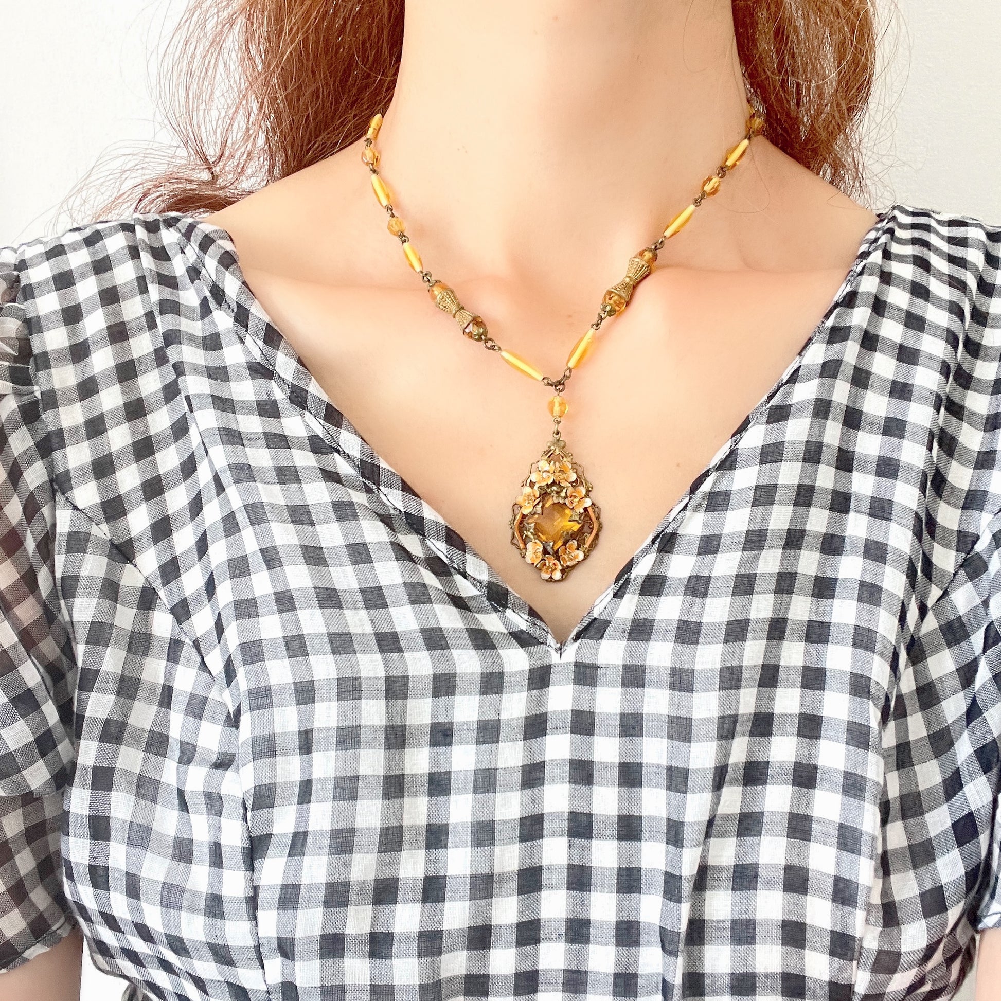 A Czech-made necklace featuring a diamond-shaped amber glass stone encircled by vivid orange enamel flowers. ダイヤ型のアンバーグラスをオレンジ色のエナメルフラワーが取り囲むチェコ製のネックレス。 