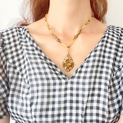 A Czech-made necklace featuring a diamond-shaped amber glass stone encircled by vivid orange enamel flowers. ダイヤ型のアンバーグラスをオレンジ色のエナメルフラワーが取り囲むチェコ製のネックレス。 