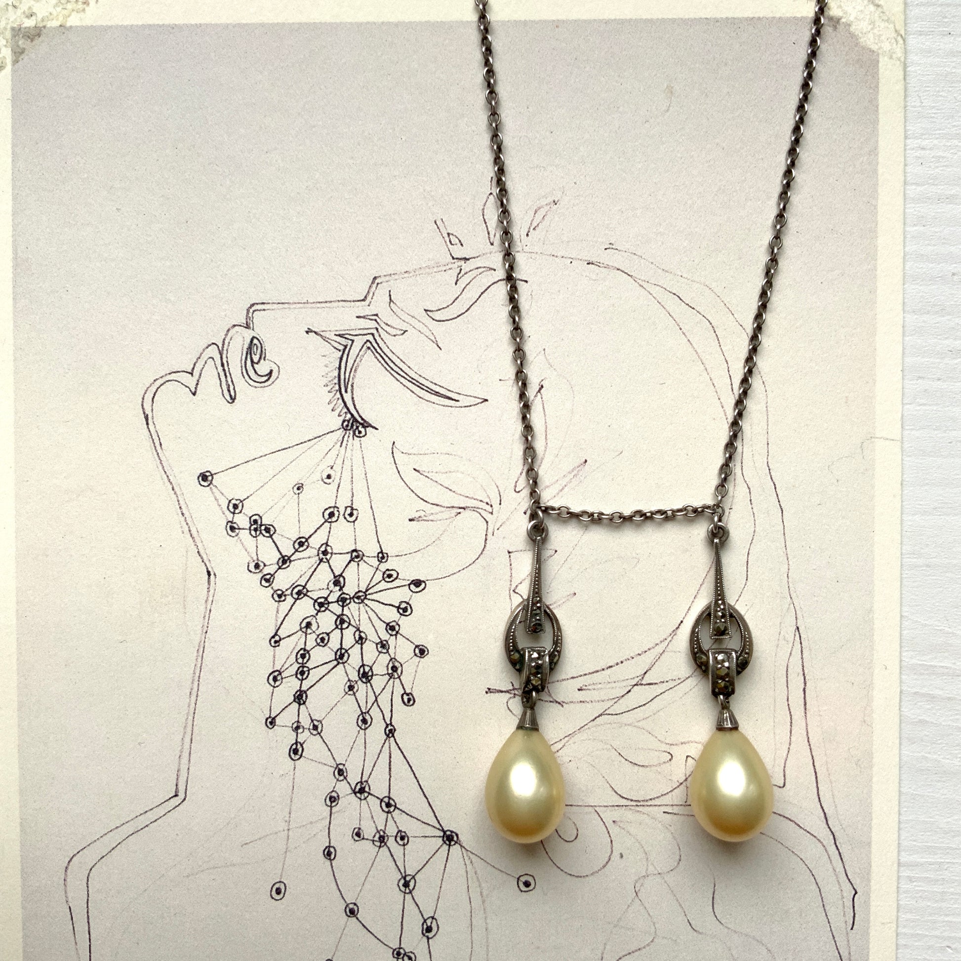 A silver necklace featuring delicate marcasite details and ivory teardrop pearls. マーカサイトの繊細なディテールとアイボリーのティアドロップパールが揺れるシルバーネックレス。