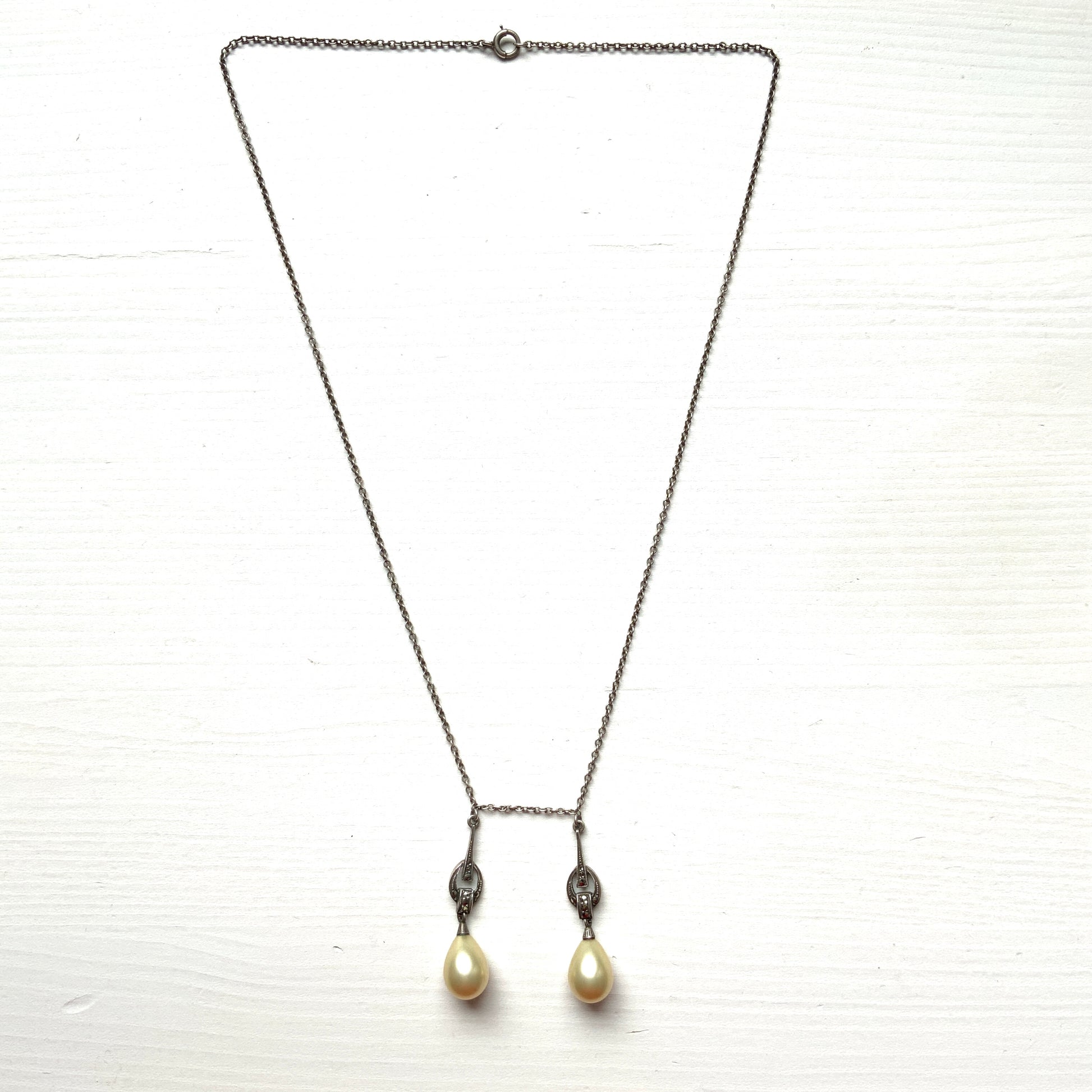 A silver necklace featuring delicate marcasite details and ivory teardrop pearls. マーカサイトの繊細なディテールとアイボリーのティアドロップパールが揺れるシルバーネックレス。