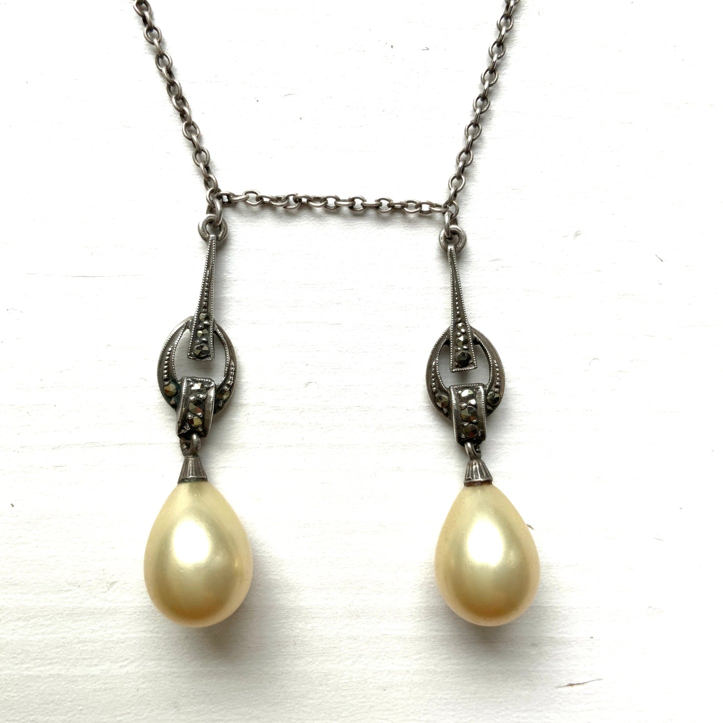 A silver necklace featuring delicate marcasite details and ivory teardrop pearls. マーカサイトの繊細なディテールとアイボリーのティアドロップパールが揺れるシルバーネックレス。