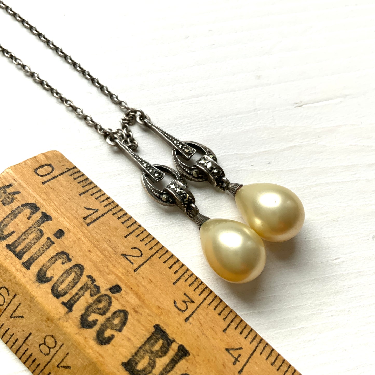 A silver necklace featuring delicate marcasite details and ivory teardrop pearls. マーカサイトの繊細なディテールとアイボリーのティアドロップパールが揺れるシルバーネックレス。