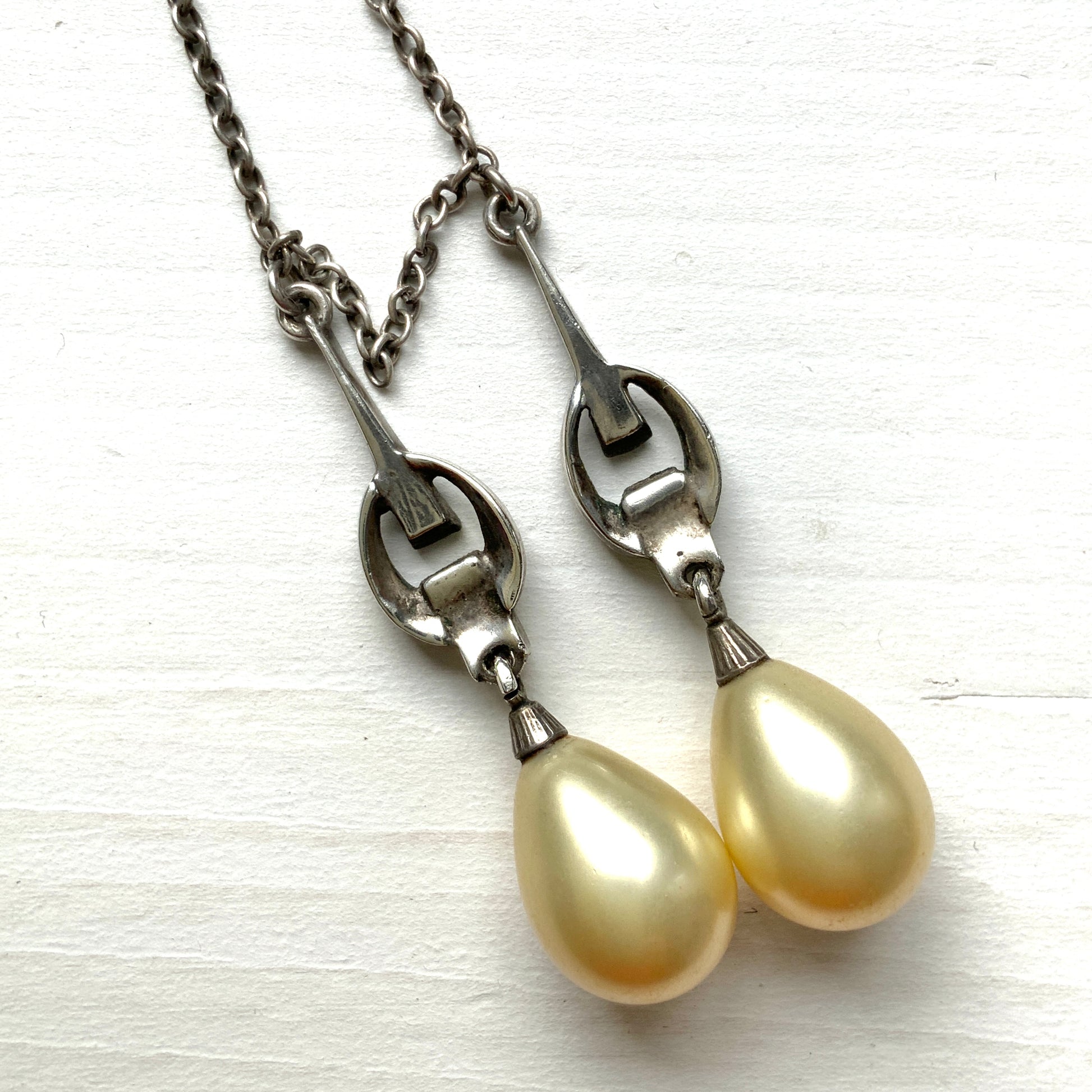 A silver necklace featuring delicate marcasite details and ivory teardrop pearls. マーカサイトの繊細なディテールとアイボリーのティアドロップパールが揺れるシルバーネックレス。