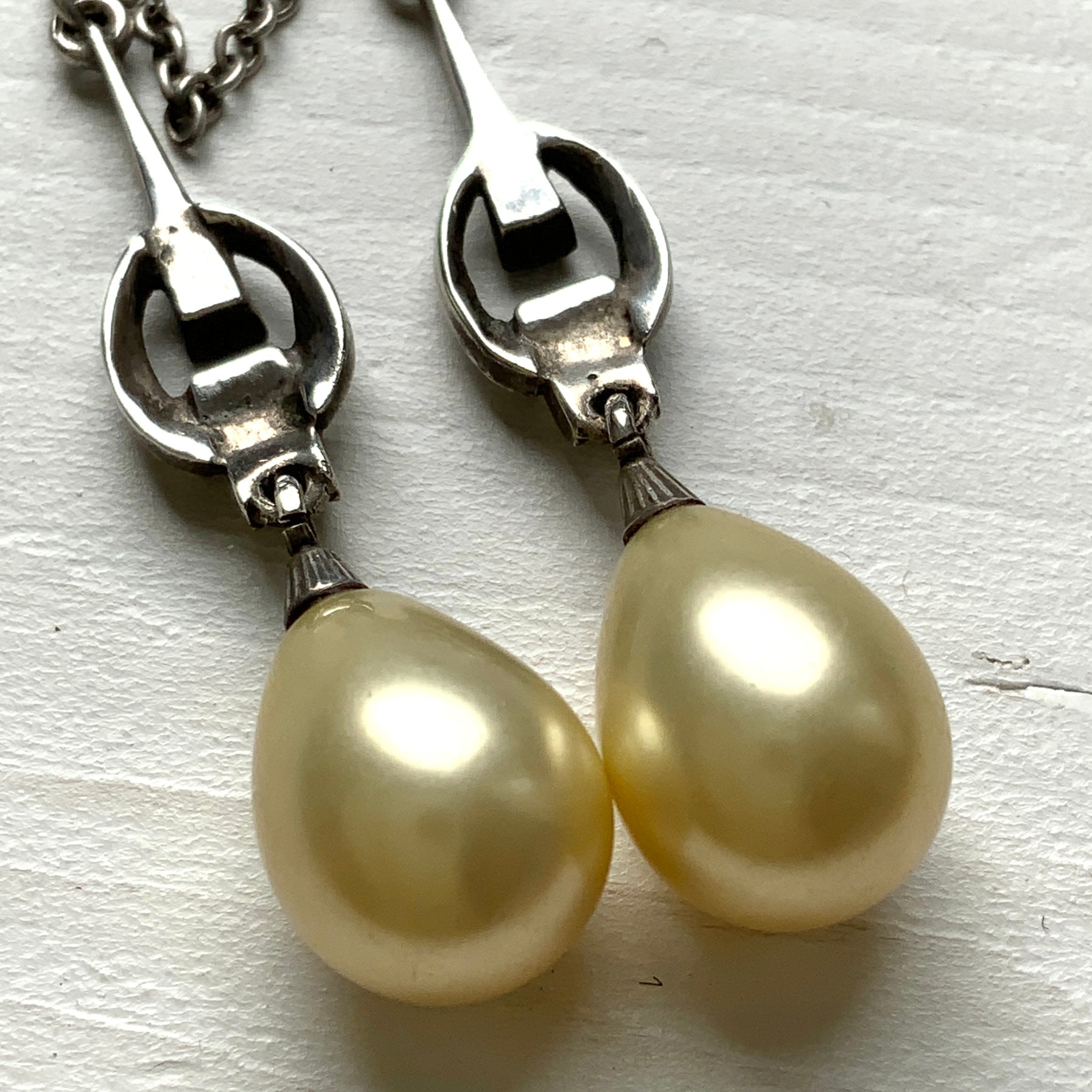 A silver necklace featuring delicate marcasite details and ivory teardrop pearls. マーカサイトの繊細なディテールとアイボリーのティアドロップパールが揺れるシルバーネックレス。