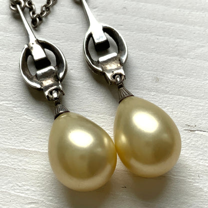 A silver necklace featuring delicate marcasite details and ivory teardrop pearls. マーカサイトの繊細なディテールとアイボリーのティアドロップパールが揺れるシルバーネックレス。
