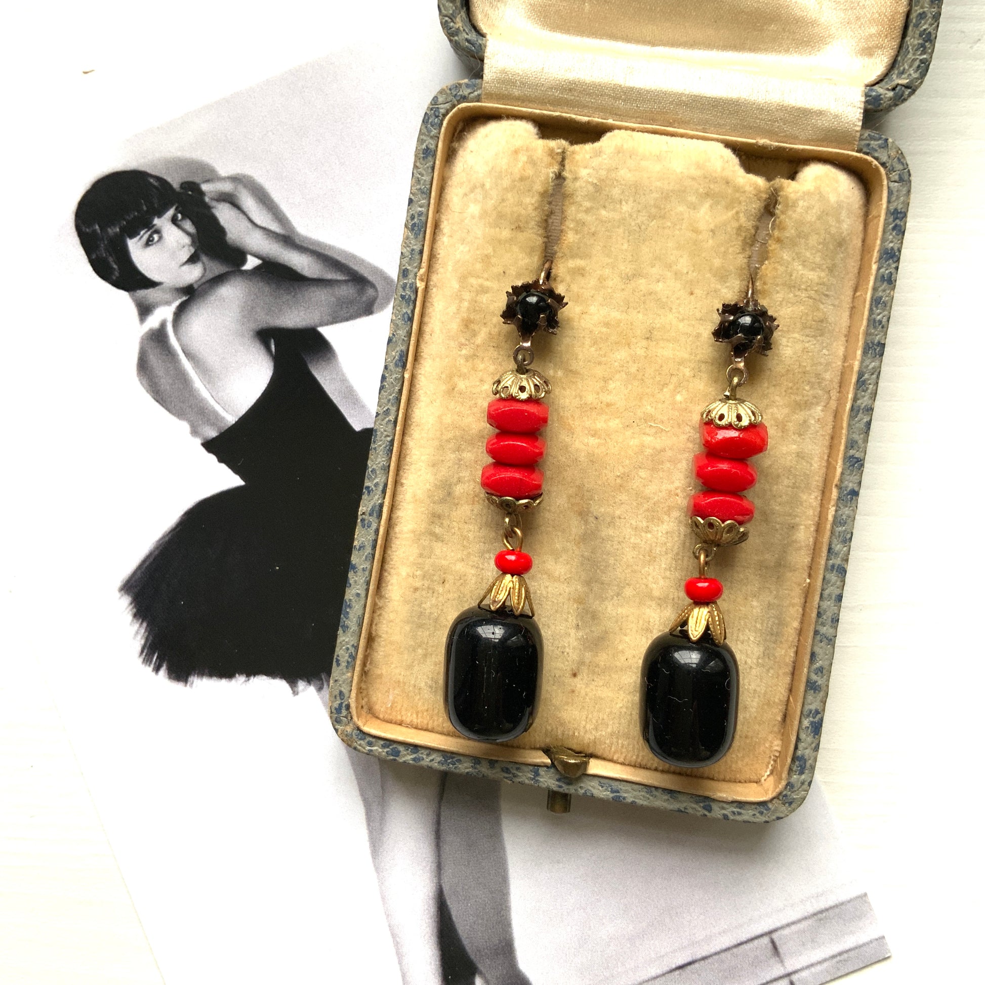 Earrings featuring stacked red glass beads with a black barrel-shaped drop that sways gracefully below. 重ねられた粒状のレッドガラスの下で、黒のバレル型ガラスが揺れるピアス。
