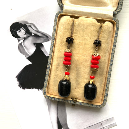 Earrings featuring stacked red glass beads with a black barrel-shaped drop that sways gracefully below. 重ねられた粒状のレッドガラスの下で、黒のバレル型ガラスが揺れるピアス。