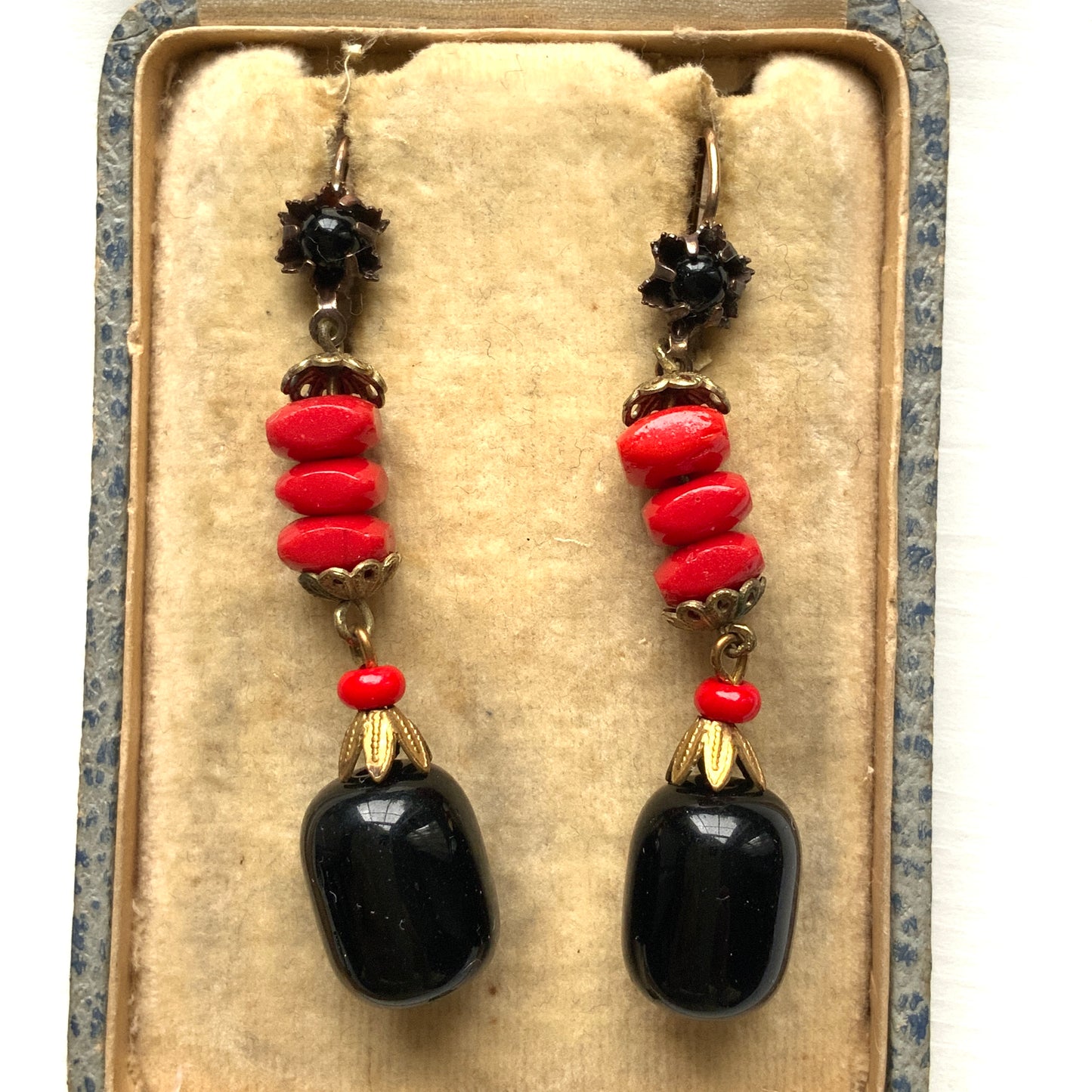 Earrings featuring stacked red glass beads with a black barrel-shaped drop that sways gracefully below. 重ねられた粒状のレッドガラスの下で、黒のバレル型ガラスが揺れるピアス。