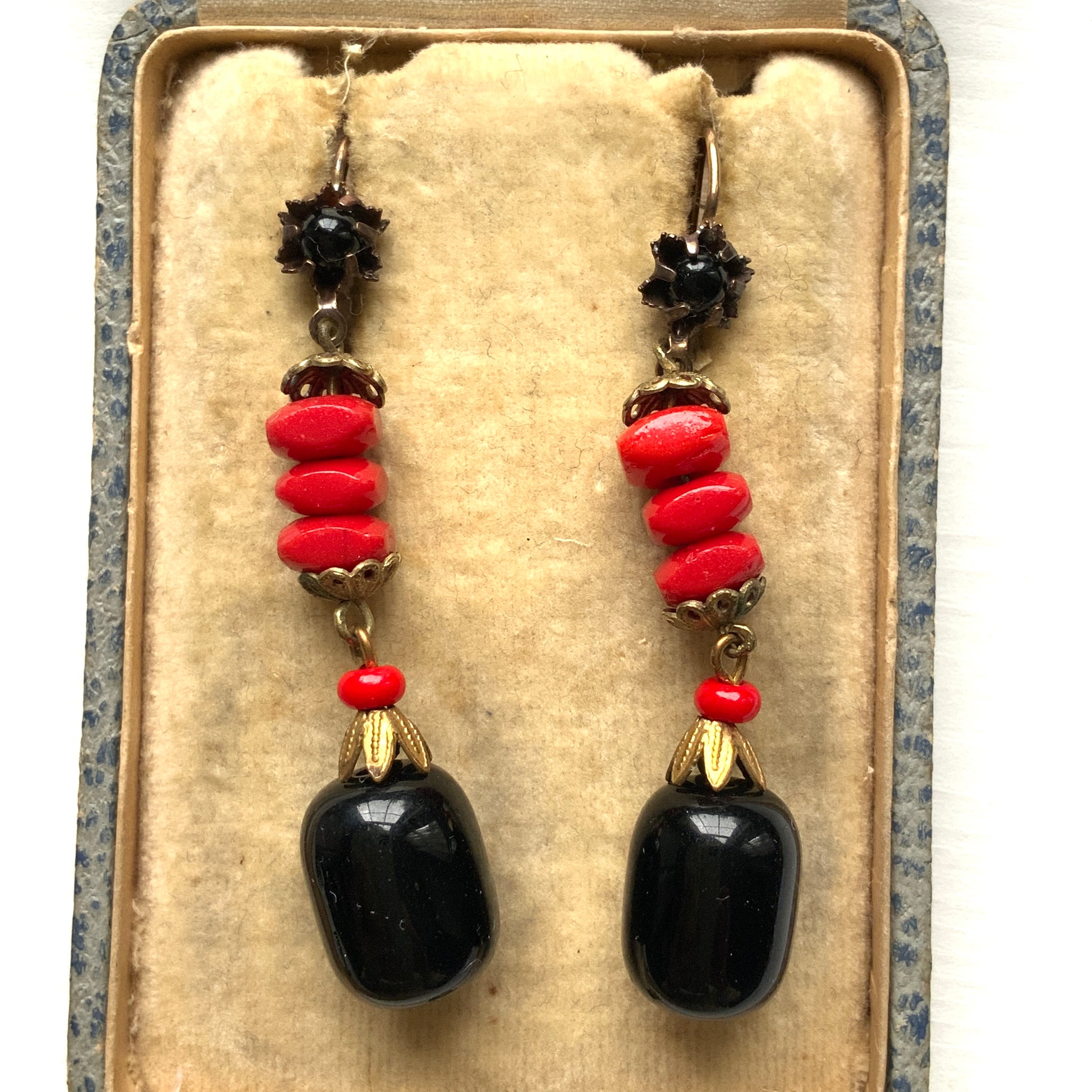 Earrings featuring stacked red glass beads with a black barrel-shaped drop that sways gracefully below. 重ねられた粒状のレッドガラスの下で、黒のバレル型ガラスが揺れるピアス。