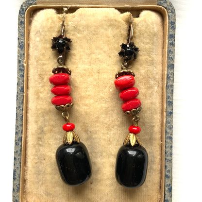 Earrings featuring stacked red glass beads with a black barrel-shaped drop that sways gracefully below. 重ねられた粒状のレッドガラスの下で、黒のバレル型ガラスが揺れるピアス。