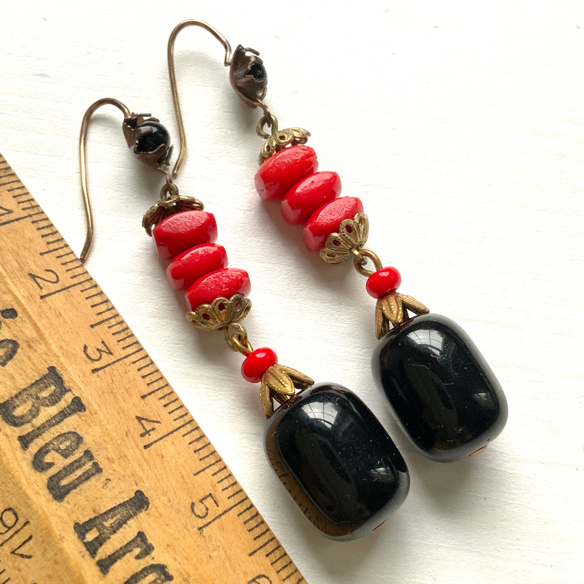 Earrings featuring stacked red glass beads with a black barrel-shaped drop that sways gracefully below. 重ねられた粒状のレッドガラスの下で、黒のバレル型ガラスが揺れるピアス。